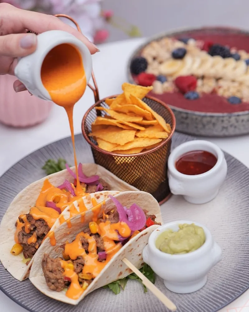 Café Rosewood Nice – tacos garnis avec sauce versée, chips tortilla, guacamole et dips sur une table de brunch
